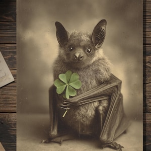 May include: Sepia-toned image of a bat holding a four-leaf clover. The bat has dark fur, large ears, and is centered in the frame. The clover is a vibrant green, contrasting with the bat's fur. The background is a soft, neutral tone.
