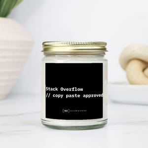 May include: A clear glass jar candle with a gold lid. The candle has a black label with the text "Stack Overflow // copy paste approved". The candle is on a white surface.