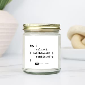 May include: A glass jar candle with a gold lid. The label displays the text "try { relax(); } catch(work) { continue(); }" in a monospace font. The candle sits on a white surface.