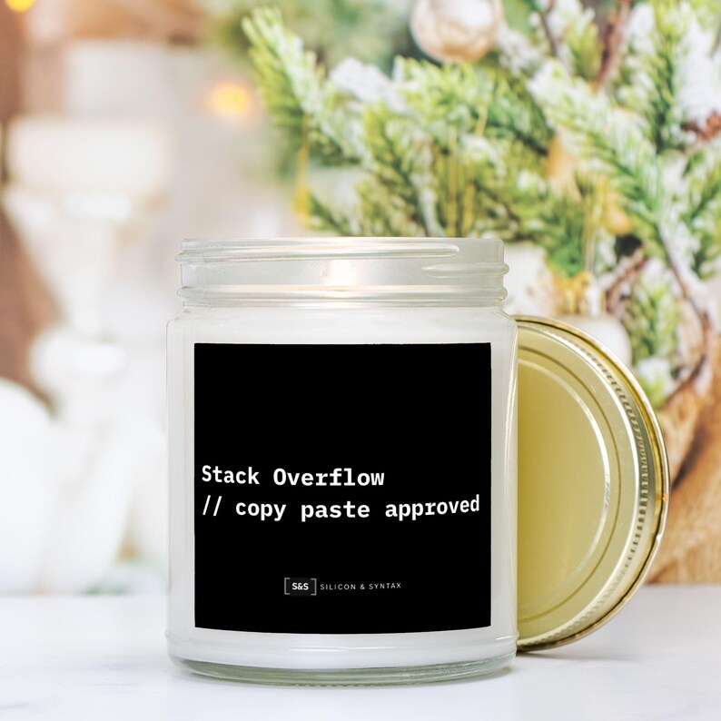 May include: A clear glass candle jar with a gold lid, featuring a black label with white text that reads "Stack Overflow // copy paste approved." The candle is likely scented and designed for home use.