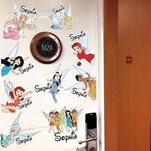 Op de afbeelding: Een witte deur versierd met kleurrijke feeënstickers, elk met de naam "Sophia" in cursief. De deur heeft ook een ronde, bruine deurplaat met het nummer "6120". Een zwarte deurklink en een kaartlezer zijn zichtbaar.