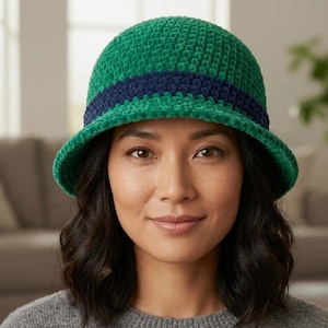 May include: A green crochet cloche hat with a dark blue band. The hat has a rounded crown and a small brim. The hat is made of a soft, textured yarn.