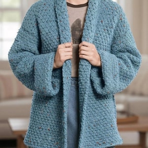 May include: A light blue, chunky knit cardigan with wide sleeves. The open-front sweater has a textured appearance with flecks of brown throughout. The cardigan is knee-length and appears to be handmade.