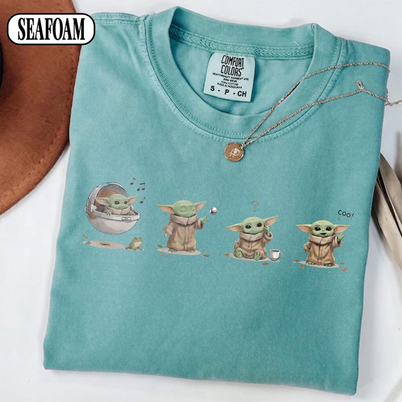 May include: Seafoam green t-shirt featuring a series of illustrations of a character from a popular science fiction franchise. The character is depicted in various poses, with the word "coo!" printed on the shirt.