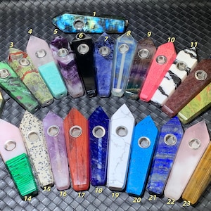 May include: A collection of twenty-three polished stone pipes, each shaped like a crystal point with a metal bowl insert. The pipes feature various colors and patterns, including blue, green, purple, pink, black, white, and brown, all numbered 1 through 23.