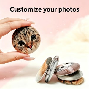 May include: A selection of round decorative stones with cat face designs. One stone, held by a hand, displays a close-up of a tabby cat's face. The text "Customize your photos" is at the top. Other stones show various cat patterns.