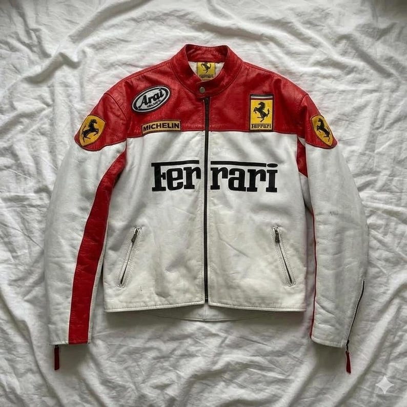 May include: A white and red Ferrari racing jacket with black lettering and logos. The jacket features a zipper closure, two front pockets, and patches including the Ferrari logo, Arai, and Michelin.