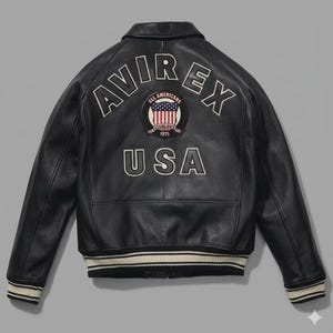 Puede incluir: Chaqueta de cuero negra con la palabra "AVIREX" en letras blancas en la espalda. Debajo, un parche con la bandera americana y la palabra "USA". La chaqueta tiene cuello y pu&ntilde;os de canal&eacute;.