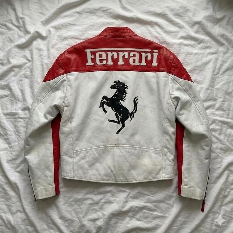 May include: White and red leather jacket with the Ferrari logo and a black prancing horse emblem on the back. The jacket has a classic racing design with red accents on the shoulders and sleeves.