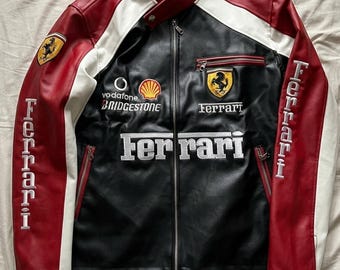 May include: A black, red, and white leather jacket with the Ferrari logo and branding. The jacket features a zip-up front, side pockets, and the word "Ferrari" embroidered on the front and sleeves. The jacket has a stand-up collar.