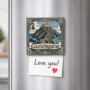 May include: A square decorative magnet featuring an illustration of the Gaztelugatxe islet with a stone bridge, a bell, and a seagull. Below the illustration, a white paper note is attached, displaying the handwritten text Love you! with a red heart.