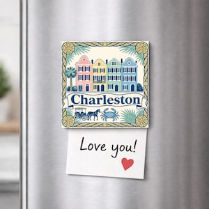 Peut inclure: Un aimant de réfrigérateur carré avec une illustration colorée de quatre maisons en rangée roses, jaunes, vertes et bleues. Le texte Charleston est imprimé sur une bannière au-dessus d'une calèche et d'un crabe. Une note blanche indique Love you! avec un cœur.