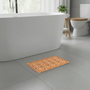 Può includere: Un tappetino da bagno rettangolare caratterizzato da un motivo ripetuto di disegni floreali arancioni e bianchi disposti in colonne verticali. Il design presenta forme botaniche simmetriche e complesse su uno sfondo arancione bruciato.