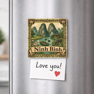 Könnte beinhalten: Ein quadratischer Kühlschrankmagnet mit einer Landschaftsillustration von Ninh Binh, Kalksteinfelsen, einem Fluss, einem Boot und einem Wasserbüffel. Ein Banner unten zeigt den Text Ninh Binh. Ein weißer Zettel mit Love you! und einem roten Herz hängt daran.