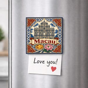 Puede incluir: Un imán decorativo cuadrado con una ilustración de las ruinas de San Pablo en Macao, una tarta de huevo portuguesa y una flor de loto rosa. La palabra Macau está impresa en una cinta. Una nota blanca con el texto Love you! y un corazón rojo.