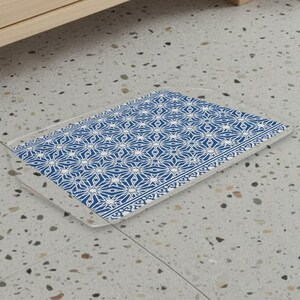 Puede incluir: Una alfombrilla rectangular con un patrón geométrico repetitivo de estrellas y líneas blancas sobre un fondo azul intenso. La alfombrilla tiene un borde fino y transparente alrededor de todo su perímetro, creando un contorno limpio y definido.