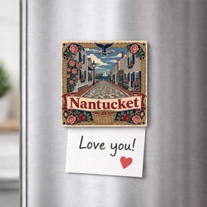 Peut inclure: Un aimant carré Nantucket illustrant une rue pavée avec des maisons, des roses, une queue de baleine et un panier. Une note en papier blanc est fixée en bas avec le texte manuscrit Love you! et une petite icône de cœur rouge en dessous.