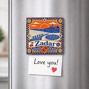 Può includere: Un magnete decorativo quadrato con un'illustrazione grafica del lungomare di Zadar al tramonto nei colori arancione, blu e bianco. Il testo Zadar è stampato in blu, accompagnato da icone di ciliegie e una conchiglia. Un foglietto dice Love you!
