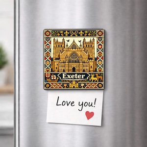 Puede incluir: Un imán rectangular con una ilustración detallada de la Catedral de Exeter, con el nombre de la ciudad debajo. El imán tiene un borde decorativo con patrones florales y geométricos. Una nota con "Love you!" y un corazón está adjunta.