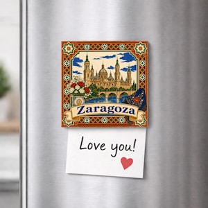 Peut inclure: Un aimant décoratif carré illustrant la basilique de Nuestra Señora del Pilar à Saragosse, en Espagne, avec un bouquet de fleurs et un châle bleu. Une note en papier blanc avec le texte manuscrit Love you! et un cœur rouge est fixée dessus.