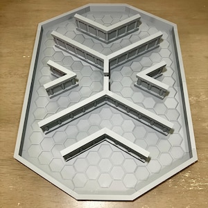 May include: A light gray, octagonal tabletop gaming board featuring a recessed hexagonal grid pattern. The board includes several raised, V-shaped wall segments with vertical pillar details arranged symmetrically across the surface.