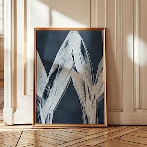 Puede incluir: Una impresión artística enmarcada con un fondo azul marino y formas botánicas abstractas blancas. La obra de arte está encerrada en un marco dorado. La impresión se exhibe contra una pared blanca y un suelo de madera. Ideal para la decoración del hogar.