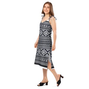 May include: A black and white patterned midi dress with tie straps. The dress features a geometric design with diamond and zigzag patterns. The dress has a slit on the side and a white hemline. The model is wearing black heels.
