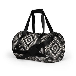 May include: Black and white duffel bag with a geometric pattern. The bag has a cylindrical shape with black handles and a shoulder strap. The pattern features diamond and rectangular shapes.