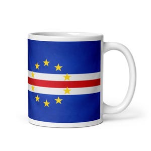 May include: White ceramic mug featuring the flag of Cape Verde. The design includes a blue background, a red and white stripe, and ten yellow stars. The mug has a white handle and a glossy finish.