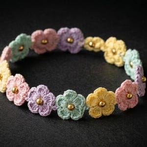 May include: A bracelet composed of a series of small, crocheted flowers in pastel shades of pink, yellow, lavender, and mint green. Each individual flower features a small, polished gold-tone metal bead at its center, creating a delicate floral chain.