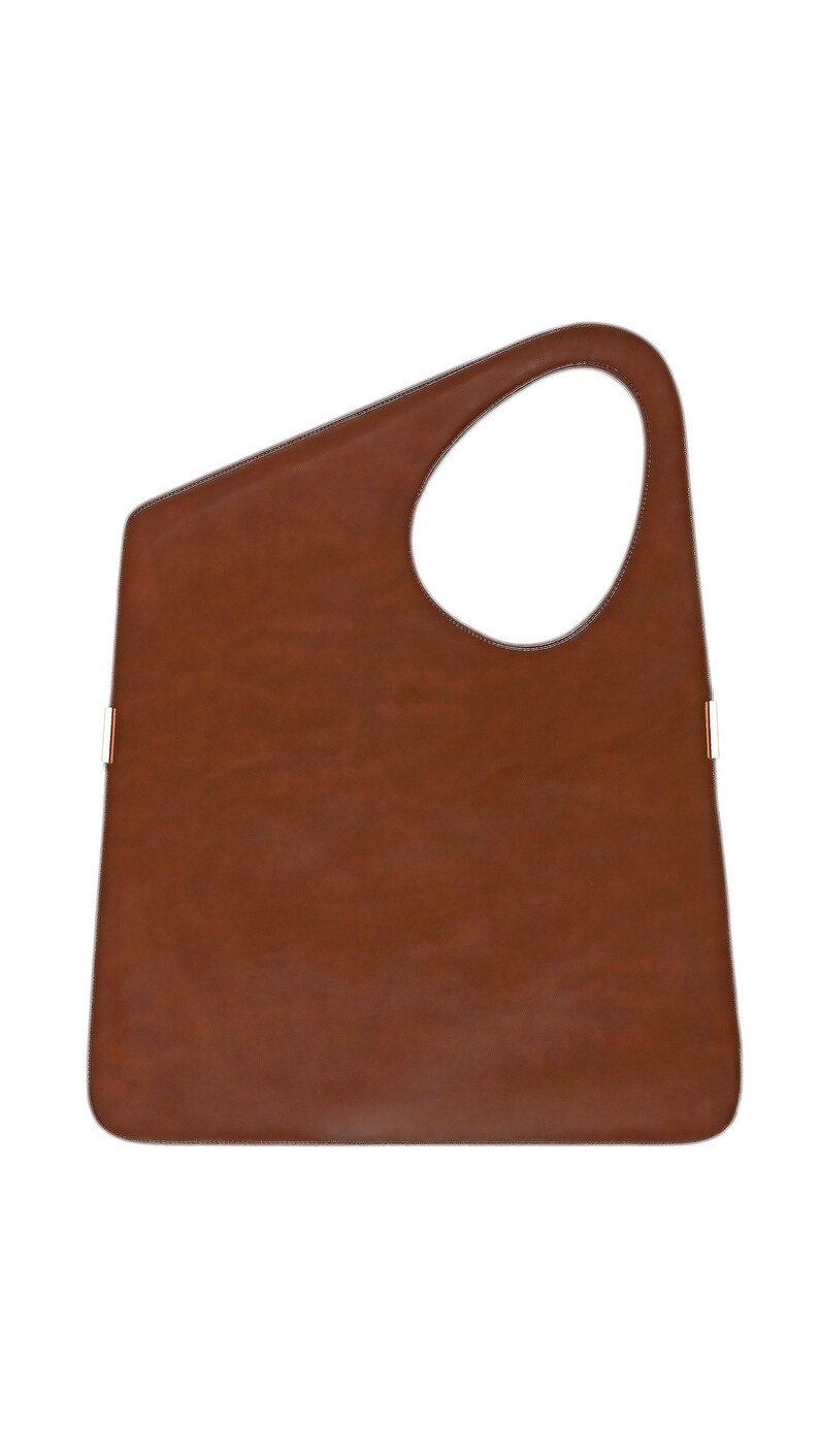 Op de afbeelding: Een bruine leren tote bag met een uniek asymmetrisch ontwerp. De tas heeft een grote, open handgreep en contrasterende stikseldetails. De tas heeft een rechthoekige vorm met een afgeronde bovenkant en een grote cirkelvormige opening.