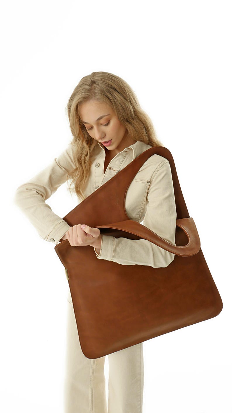 Minimalist oversized vegan leather tote with sculptural asymmetrical handle and modern architectural silhouette. This spacious extra large tote bag functions as a relaxed slouchy leather bag perfect for everyday carry. Designed as a versatile commuter bag, it easily fits a laptop as a leather macbook bag while maintaining the effortless elegance of a leather slouchy bag and the capacity of a giant leather bag.