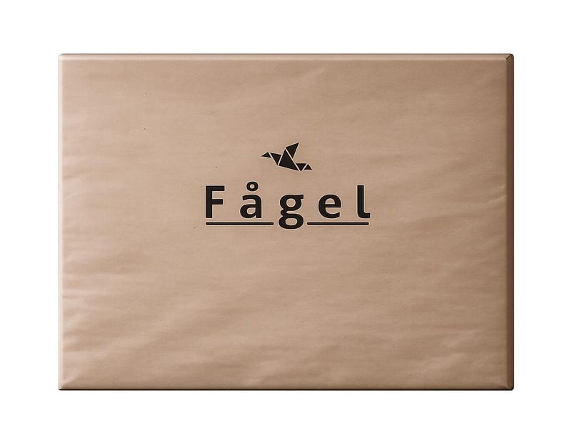 Op de afbeelding: Een rechthoekig pakket verpakt in bruin papier. Het pakket heeft het woord "F&aring;gel" in zwarte letters, met een gestileerd vogelpictogram erboven. Het papier heeft een licht getextureerd uiterlijk.