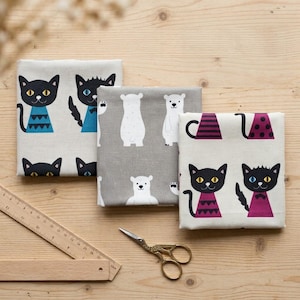 Peut inclure: Trois carrés de tissu pliés avec des motifs d'animaux. Un carré présente des chats noirs avec des accents bleus et turquoise sur fond clair. Un autre est gris avec des ours polaires blancs. Le troisième a des chats noirs avec des accents violets.