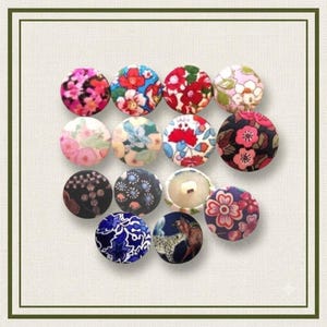 Pode incluir: Uma coleção de catorze botões circulares cobertos de tecido dispostos em um grupo. Cada botão apresenta um padrão único, incluindo vários designs florais em vermelho, rosa, azul e verde, bem como estampas geométricas e um motivo animal.