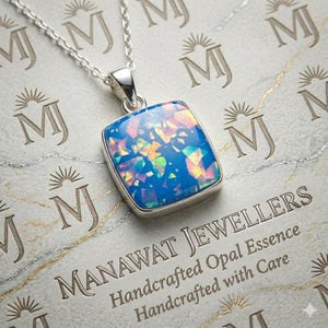 Op de afbeelding: Een zilveren ketting met een vierkante hanger met een levendige blauwe opaal met kleurrijke iriserende insluitsels. De hanger is gezet in een zilveren rand en hangt aan een fijne zilveren ketting. De achtergrond heeft de tekst "MANAWAT JEWELLERS".