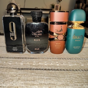 May include: Four rectangular and cylindrical perfume bottles standing in a row. The first is a clear glass bottle labeled 9pm Afnan. The second is a black bottle labeled Hawas Black. The third is a matte brown bottle labeled Asad Bourbon. The fourth is a teal bottle labeled Ramad Oriental.