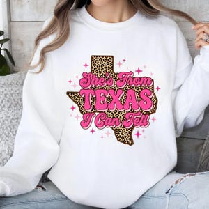 Puede incluir: Sudadera blanca con un gr&aacute;fico de Texas rosa y estampado de leopardo con el texto "She's From Texas I Can Tell". El dise&ntilde;o incluye estrellas rosas. Una parte superior casual y c&oacute;moda.