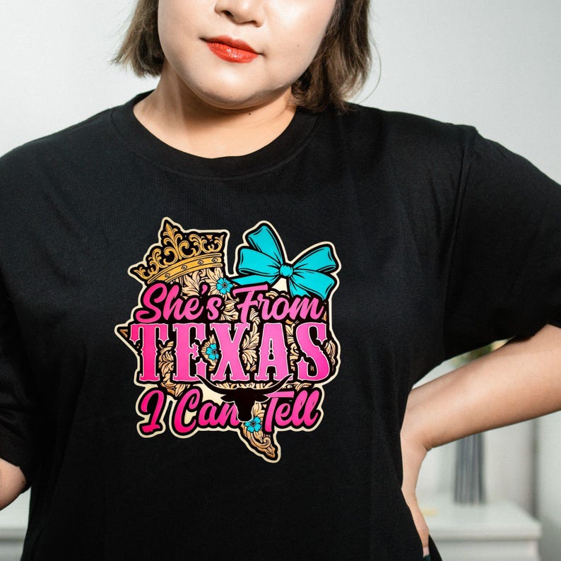 Puede incluir: Camiseta negra con un gr&aacute;fico colorido que dice "She's From Texas I Can Tell". El dise&ntilde;o incluye una corona, un lazo azul y el contorno de Texas en rosa y amarillo. Ropa casual.