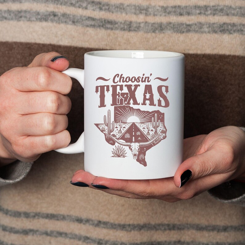 Puede incluir: Taza de cer&aacute;mica blanca con el texto "Choosin' TEXAS" en marr&oacute;n, con un estilo vintage. El dise&ntilde;o incluye un contorno de Texas con una carretera, cactus y una calavera de cuernos largos. La taza tiene un asa blanca.
