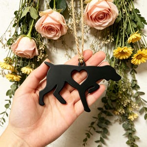 Puede incluir: Adorno negro en forma de perro con un corazón recortado. Cuelga de una cuerda de hilo natural. El fondo presenta rosas rosas y flores amarillas.