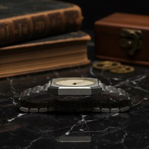 May include: A silver-toned wristwatch with a rectangular face and a light-colored dial. The watch has a metal band and is displayed on a black marble surface. The watch is a classic accessory.