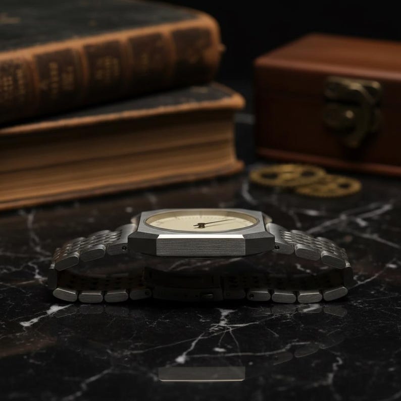 May include: A silver-toned wristwatch with a rectangular face and a light-colored dial. The watch has a metal band and is displayed on a black marble surface. The watch is a classic accessory.
