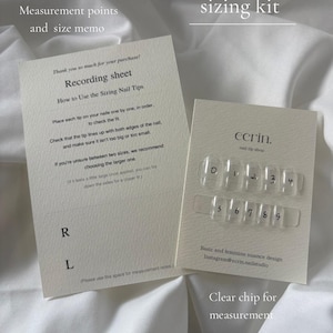 Op de afbeelding: Een maattabelset voor kunstnagels met een crèmekleurig opnameblad met instructies en een aparte kaart met tien doorzichtige plastic nageltips, genummerd van nul tot negen, voorzien van het merklabel ecrin. nail tip shop.