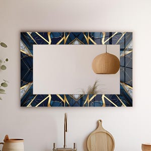 May include: Rectangular wall mirror with a geometric design. The frame features a navy blue and gold pattern with a marble-like texture. The mirror is hanging above a kitchen sink, with a wooden cutting board and bowl visible.