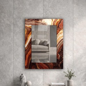 May include: A rectangular wall mirror featuring a decorative frame with a swirling, multi-toned brown and cream agate-like pattern. The reflective glass surface displays a clear view of a sofa, capturing the surrounding interior space.