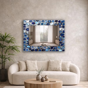 Puede incluir: Espejo de pared rectangular con marco de piedras de &aacute;gata azules y blancas. El espejo refleja una habitaci&oacute;n con ventana y cortinas. El espejo est&aacute; montado en una pared de color neutro sobre un sof&aacute; crema.