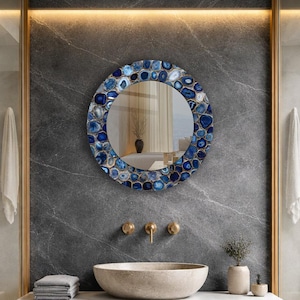 Puede incluir: Espejo redondo con borde de mosaico de piedras azules y blancas. El espejo est&aacute; montado en una pared de m&aacute;rmol gris sobre un lavabo de piedra con grifos dorados. Dise&ntilde;o de ba&ntilde;o moderno.