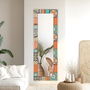 May include: A tall, rectangular full-length mirror featuring a decorative frame composed of various square tiles. The tiles display a repeating pattern of intricate geometric and floral motifs in vibrant shades of orange, teal, and dark brown.