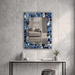 Puede incluir: Espejo rectangular con un marco adornado con piedras de &aacute;gata azules y blancas. El espejo refleja una habitaci&oacute;n con un sof&aacute;. El espejo est&aacute; montado en una pared gris sobre una mesa negra con objetos decorativos y una bolsa de cuero negra.
